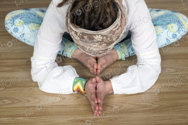 High angle view of woman wearing white blouse and headscarf sitting on floor in yoga pose.