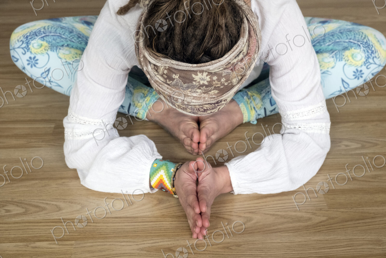 High angle view of woman wearing white blouse and headscarf sitting on floor in yoga pose.