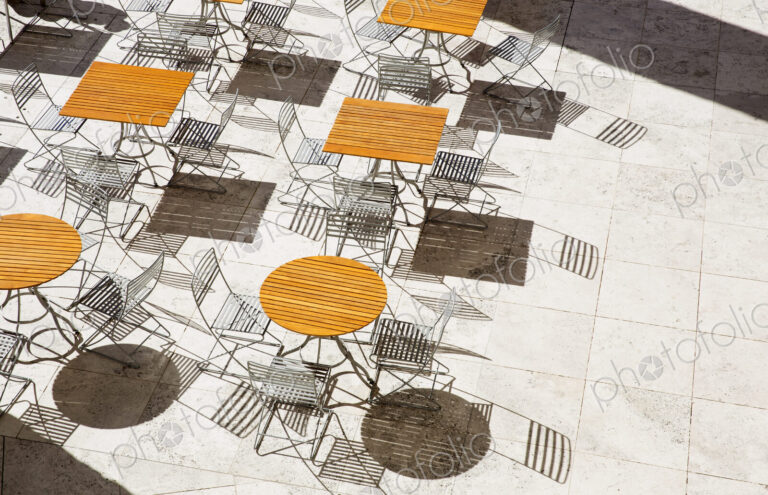 High angle view of wooden tables and metal folding chairs casting shadows onto brown…