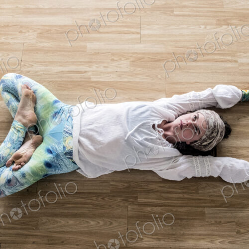 High angle view of young woman wearing headscarf and white blouse lying on her back on…