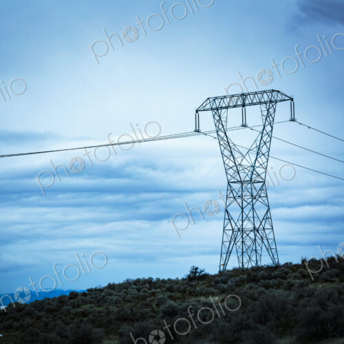 High transmission tower and wires in a rural landscape against a blue sky.