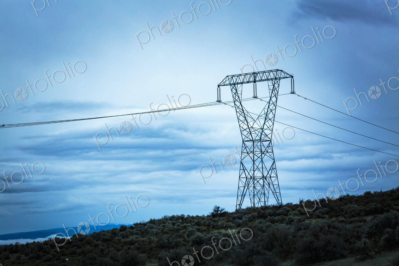 High transmission tower and wires in a rural landscape against a blue sky.