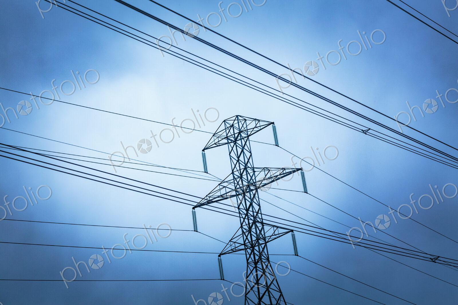 High transmission tower and wires seen from a low angle, overhead power cables.