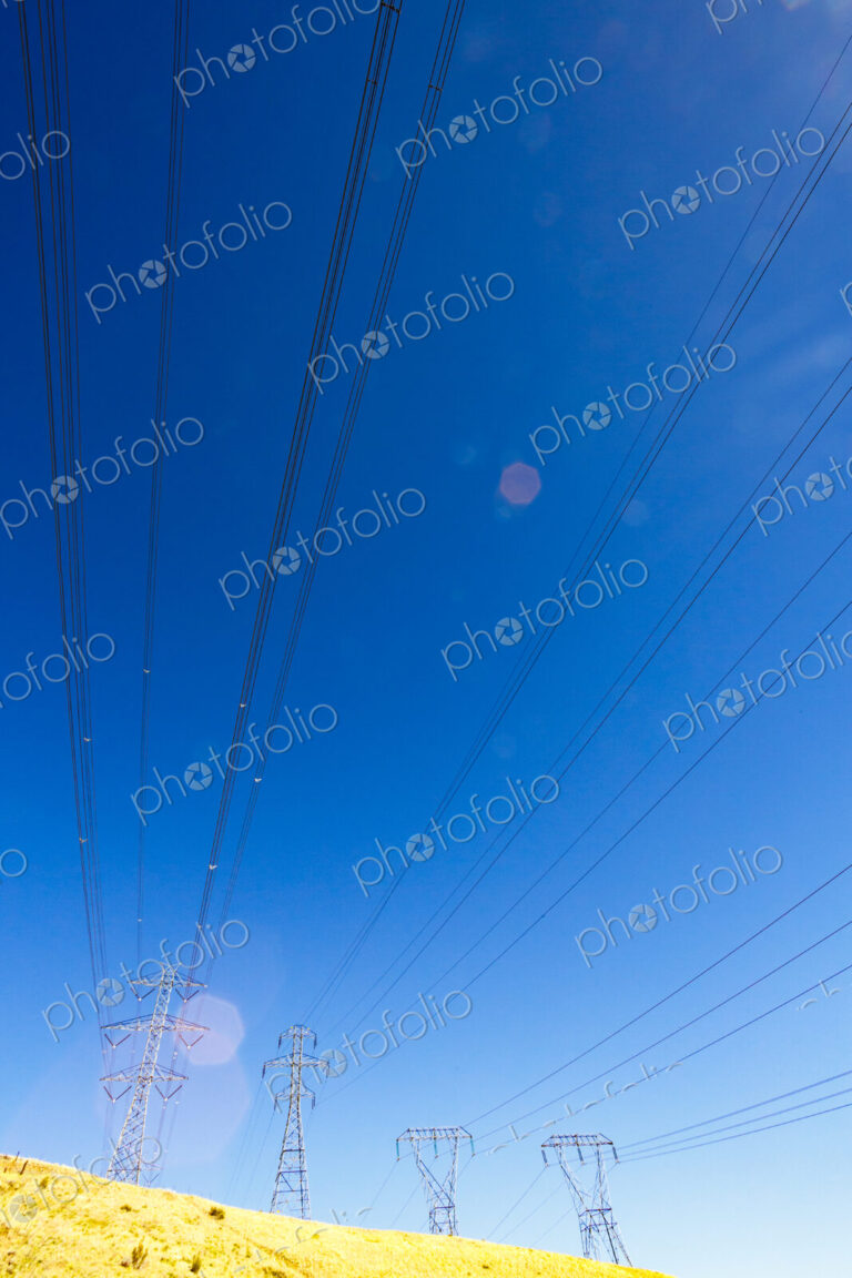 High transmission towers and lines over a dry hillside.