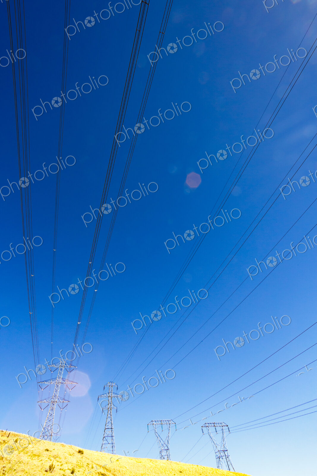 High transmission towers and lines over a dry hillside.