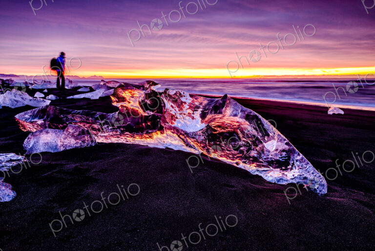 Hiker admiring glaciers on beach reflecting sunset sky