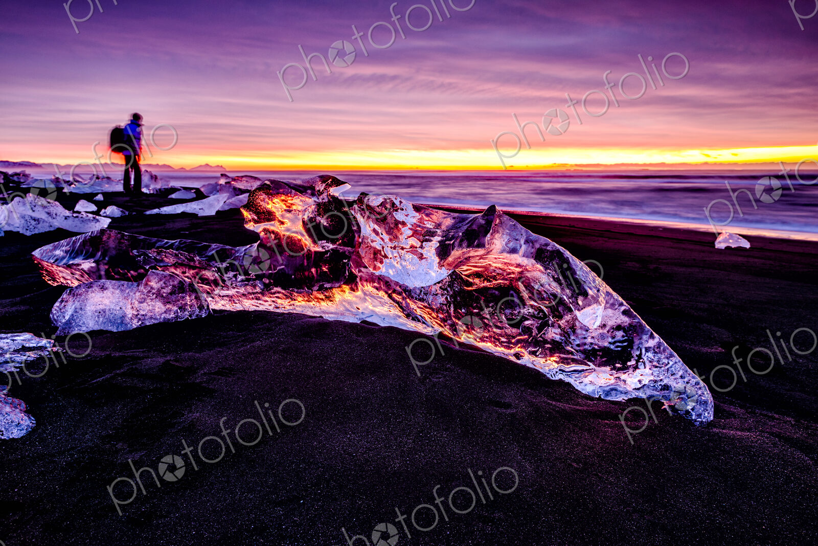 Hiker admiring glaciers on beach reflecting sunset sky