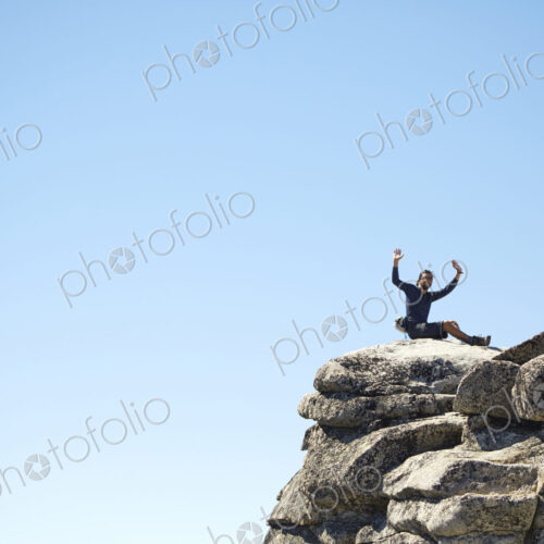Hiker cheering on rocky hilltop under blue sky Hiker cheering on rocky hilltop under blue sky