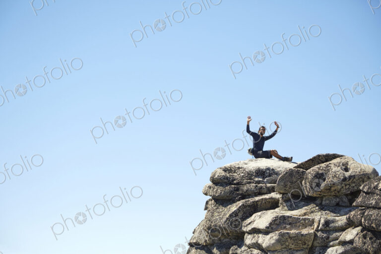 Hiker cheering on rocky hilltop under blue sky