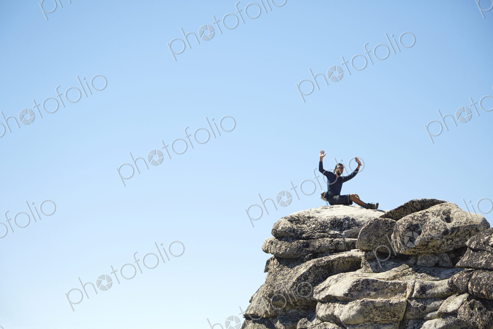 Hiker cheering on rocky hilltop under blue sky