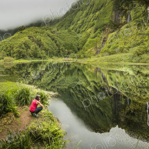 Hiker crouching at still lake in remote mountains Hiker crouching at still lake in remote mountains