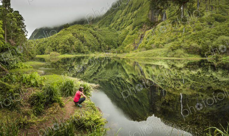Hiker crouching at still lake in remote mountains