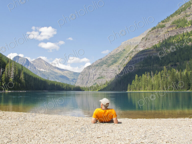 Hiker laying near mountain lake, Glacier National Park, Montana, United States