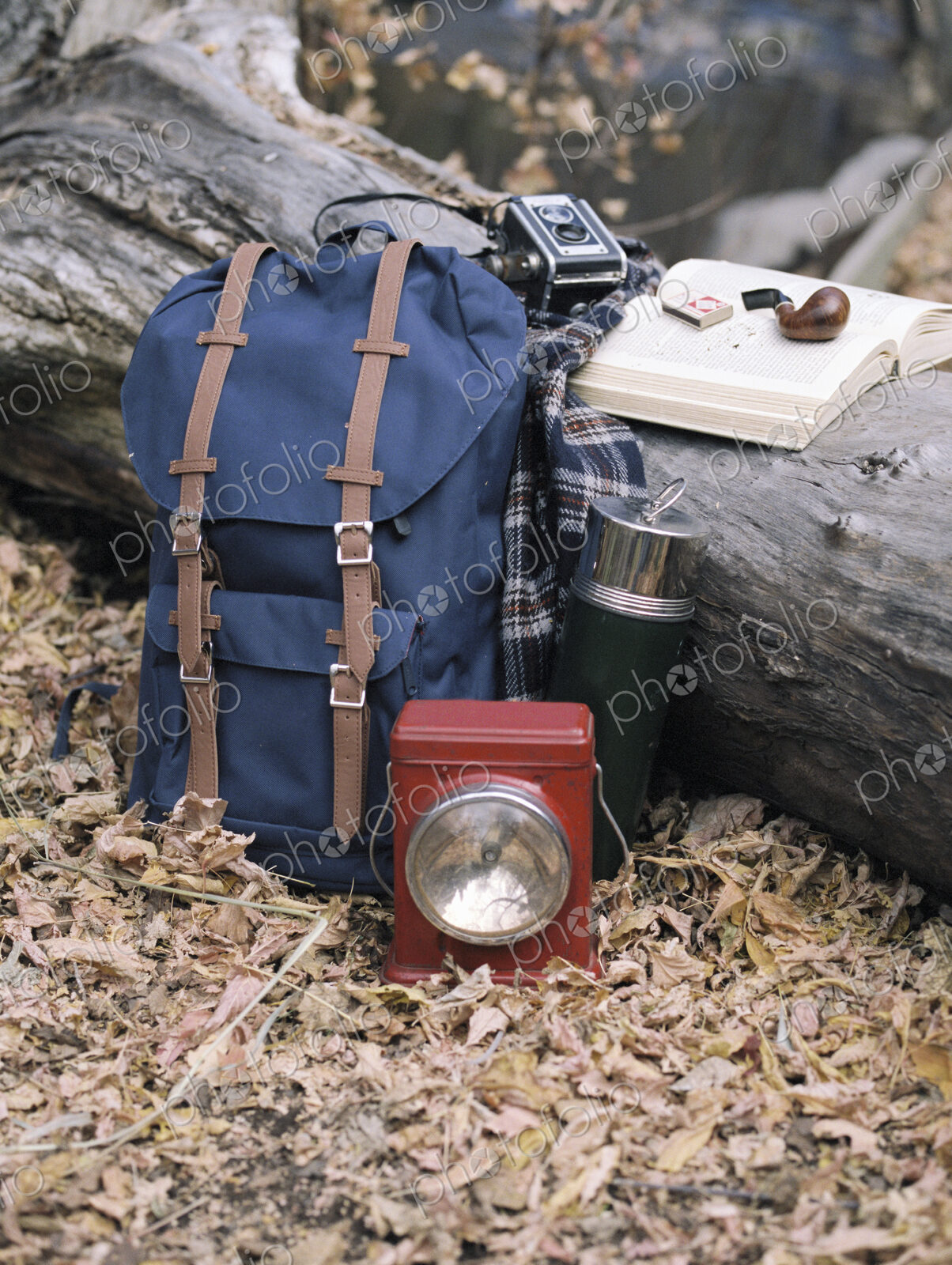Hiking equipment, a backpack, torch, flask and camera by a tree trunk. A pipe lying on…