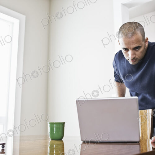 Hipanic man checking his laptop computer at the dinning room table in a new home. Hipanic man checking his laptop computer at the dinning room table in a new home.