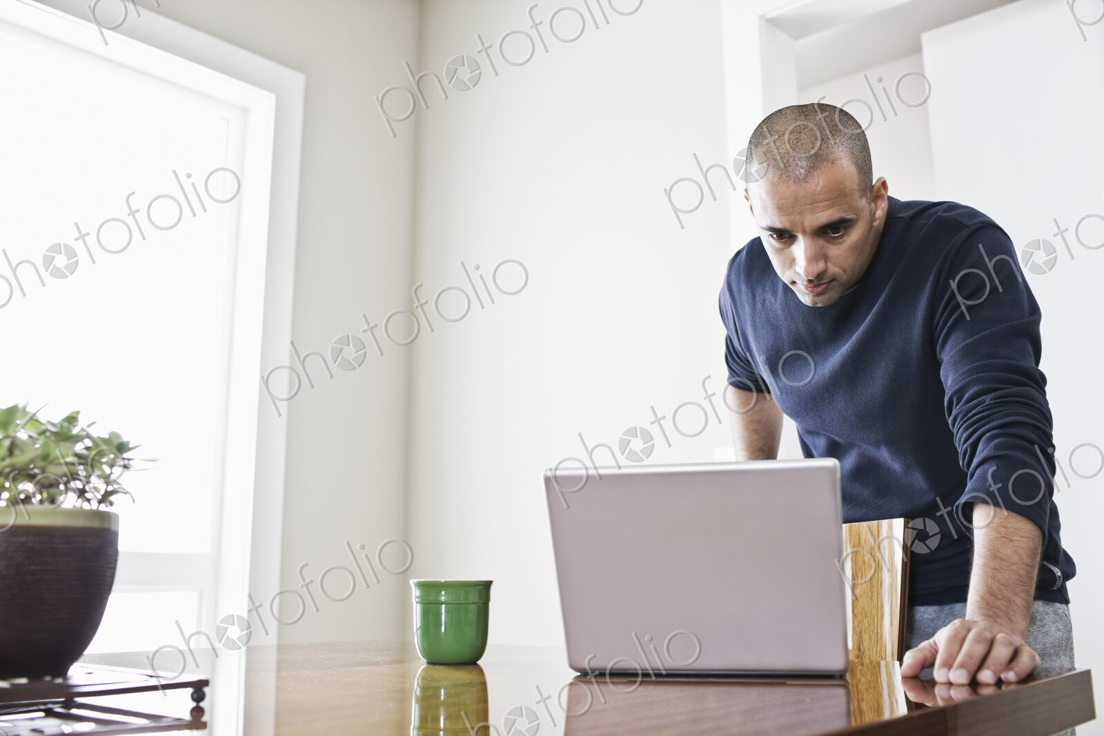 Hipanic man checking his laptop computer at the dinning room table in a new home.