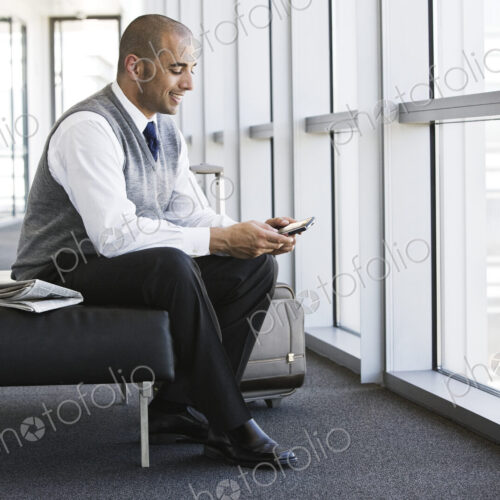 Hispanic businessman texting while sitting on a bench in a business office lobby.