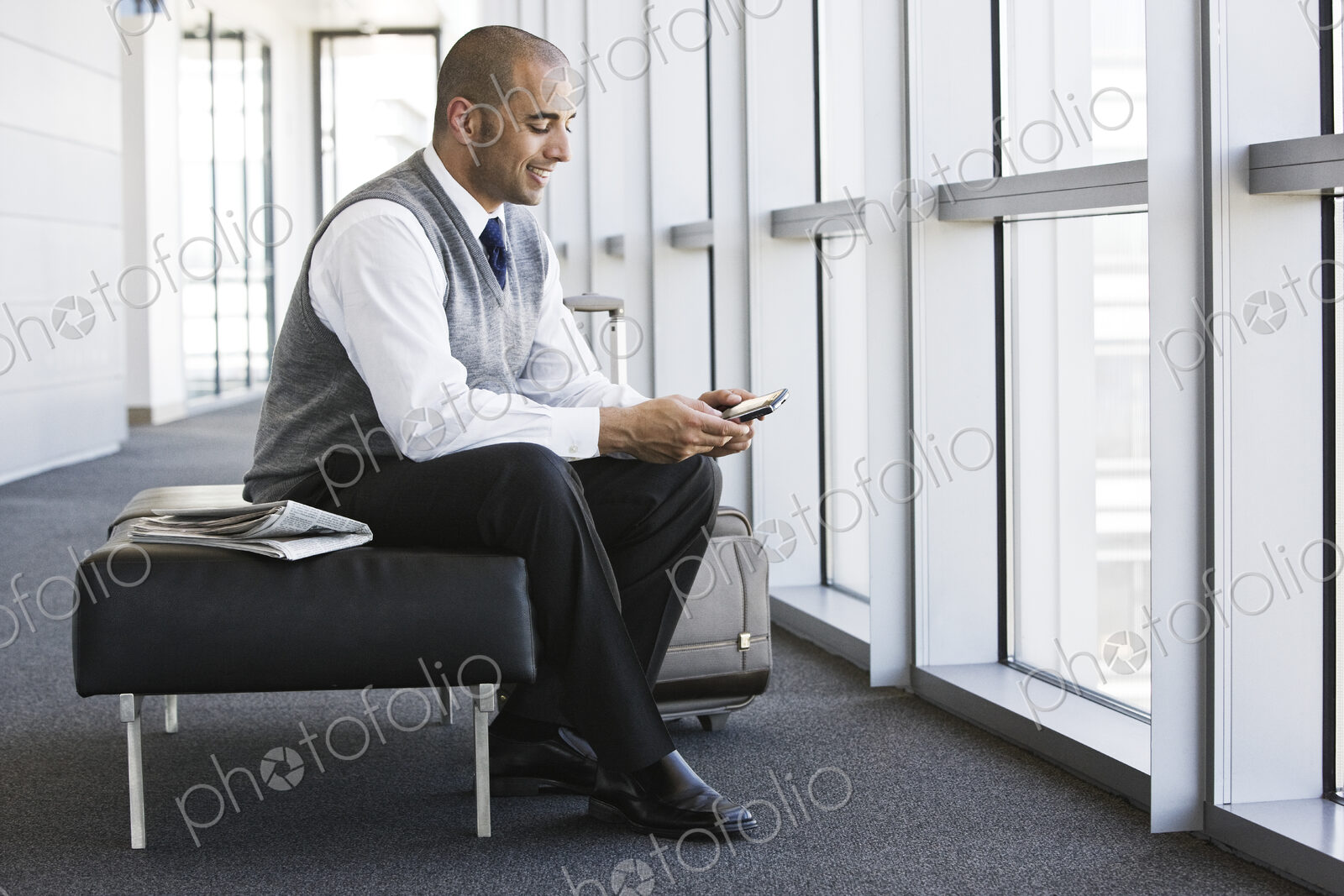 Hispanic businessman texting while sitting on a bench in a business office lobby.