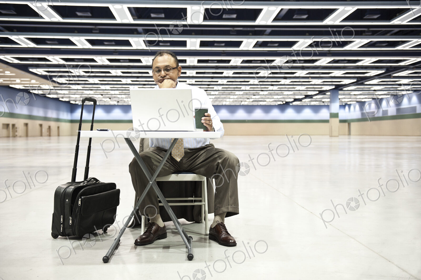Hispanic businessman using laptop computer at small desk in a large space