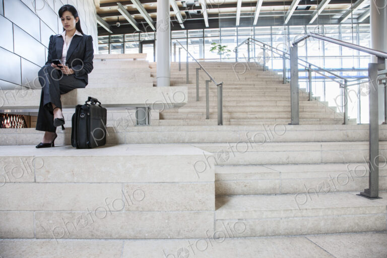 Hispanic businesswoman sitting on stairs in the lobby of a large office building.