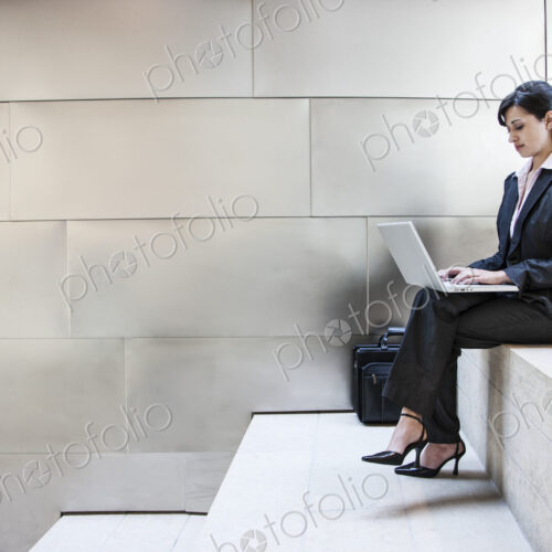Hispanic businesswoman sitting on stairs in the lobby of a large office building.
