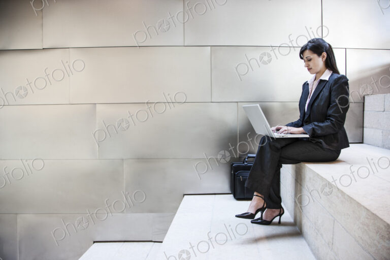 Hispanic businesswoman sitting on stairs in the lobby of a large office building.
