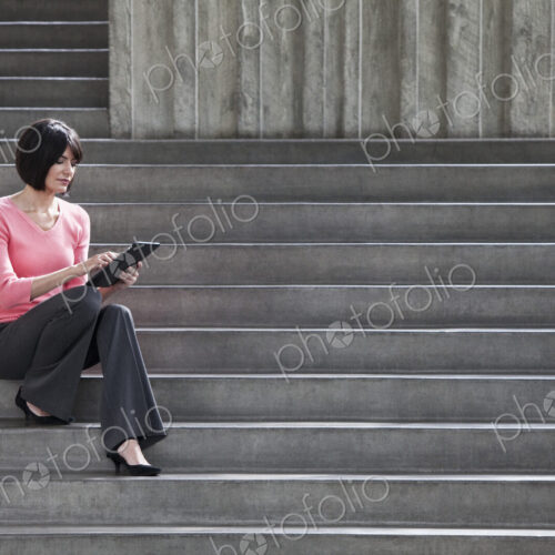 Hispanic businesswoman working on a notebook computer while sitting on steps in a… Hispanic businesswoman working on a notebook computer while sitting on steps in a…