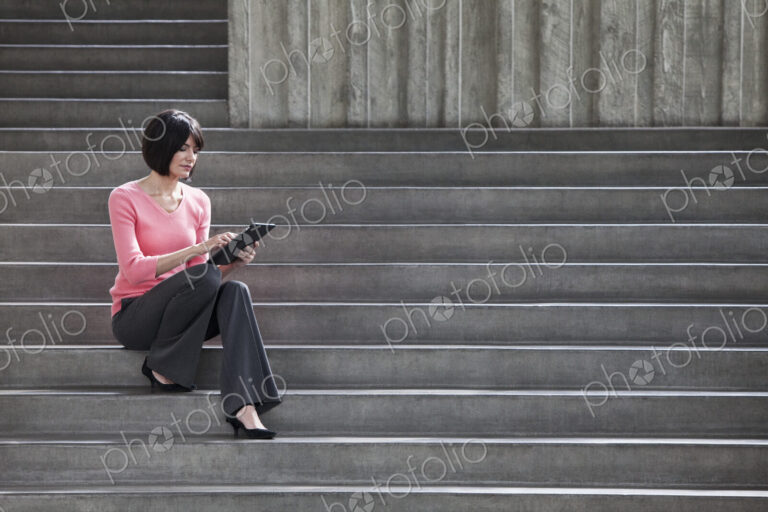 Hispanic businesswoman working on a notebook computer while sitting on steps in a…