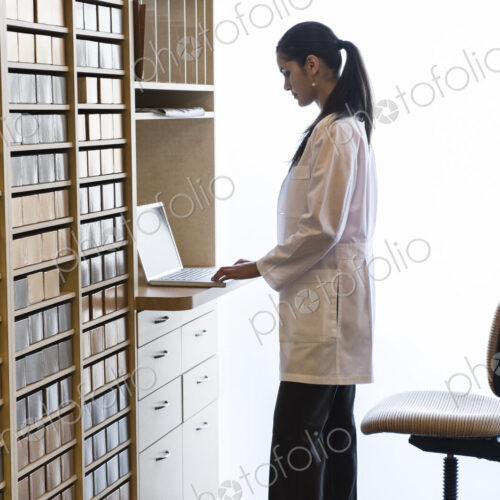 Hispanic female dentist working on a laptop computer in a cabinet file area of a… Hispanic female dentist working on a laptop computer in a cabinet file area of a…