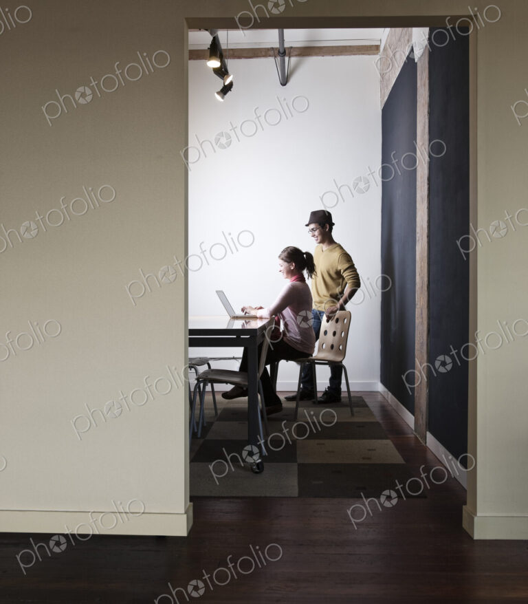 Hispanic male and caucasian female working on a laptop computer in a small conference…