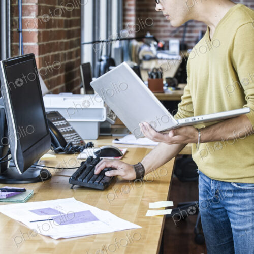 Hispanic male at his office workstation in a creative office. Hispanic male at his office workstation in a creative office.