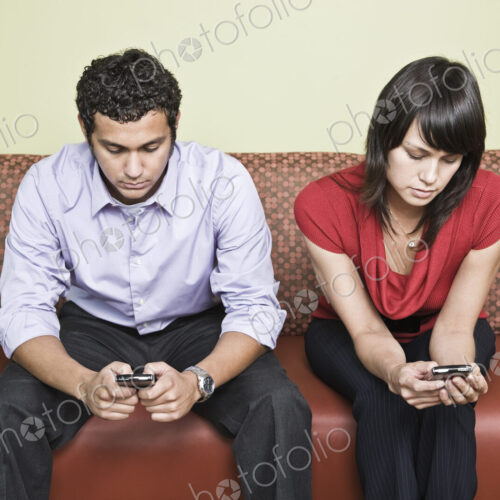 Hispanic man and caucasian woman each on a cell phone in an office.