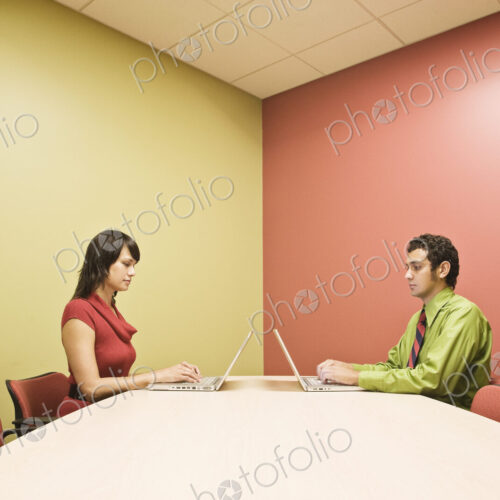 Hispanic man and caucasian woman on lap top computers in a colorful office conference… Hispanic man and caucasian woman on lap top computers in a colorful office conference…