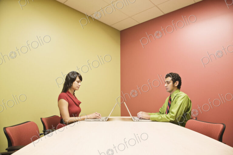Hispanic man and caucasian woman on lap top computers in a colorful office conference…