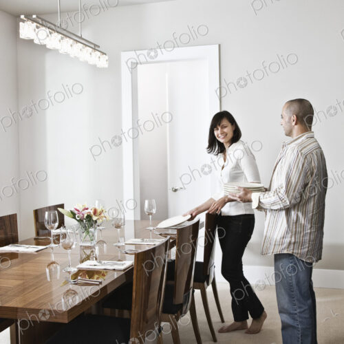 Hispanic man and woman doing place settings at their dinning room table in a new home.
