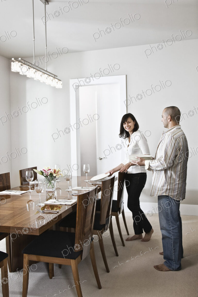 Hispanic man and woman doing place settings at their dinning room table in a new home.