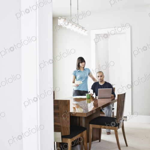 Hispanic man and woman looking at a laptop computer on the dinning room table of a new… Hispanic man and woman looking at a laptop computer on the dinning room table of a new…