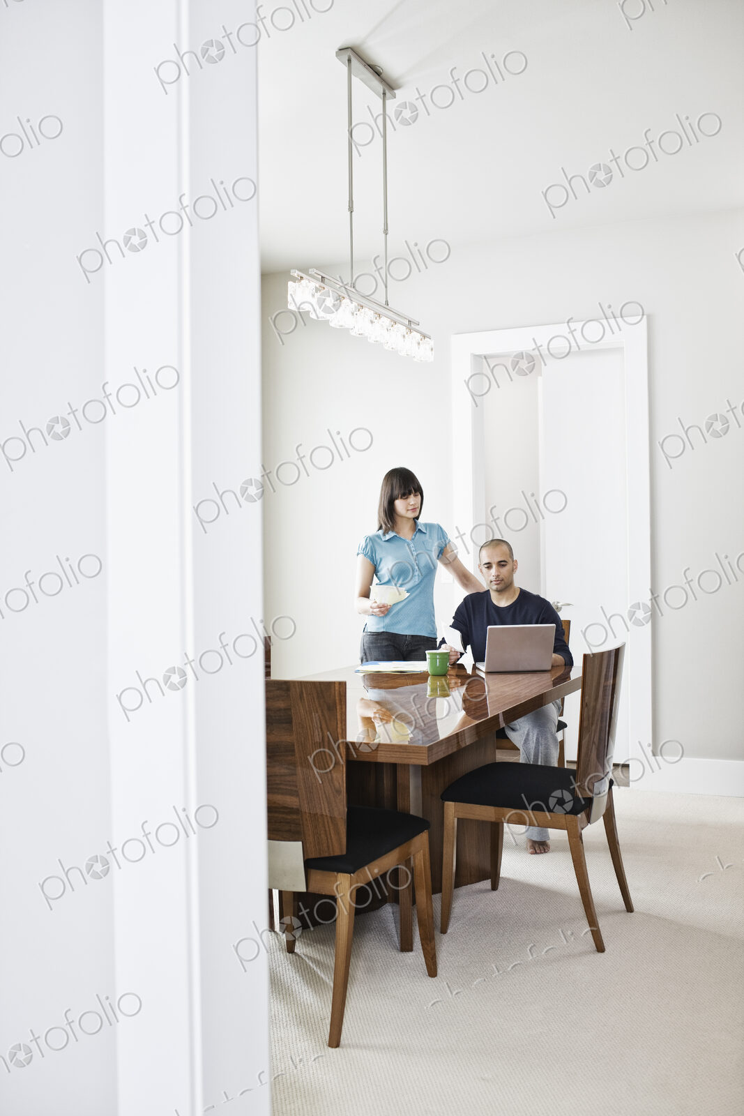 Hispanic man and woman looking at a laptop computer on the dinning room table of a new…