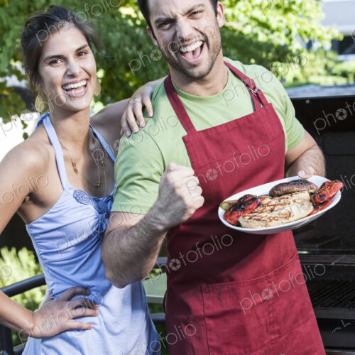 Hispanic man and woman standing at an outdoor grill holding freshly cooked food. Hispanic man and woman standing at an outdoor grill holding freshly cooked food.