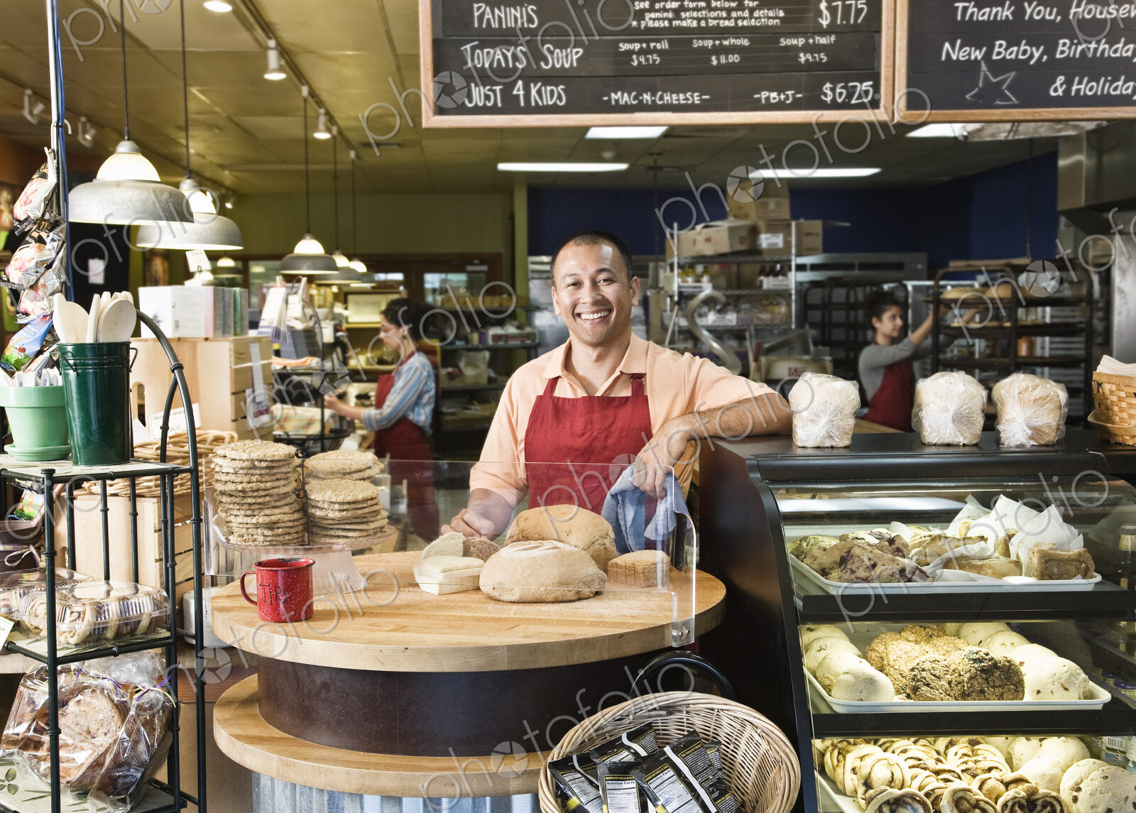 Hispanic man baker and employees in the backgrtound of the bakery.