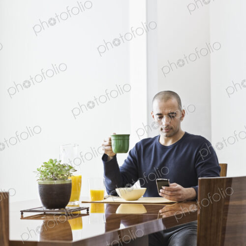 Hispanic man checking his phone at the dinning room table in a new home. Hispanic man checking his phone at the dinning room table in a new home.