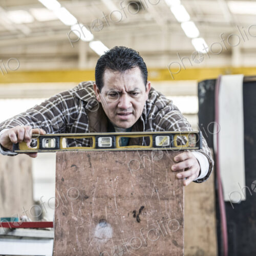 Hispanic man factory worker using a level on a metal part in a sheet metal factory.