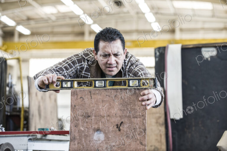 Hispanic man factory worker using a level on a metal part in a sheet metal factory.