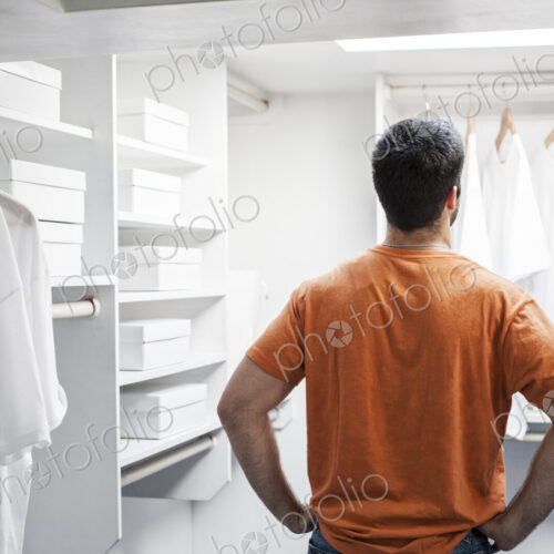 Hispanic man in a closet full of white clothes.
