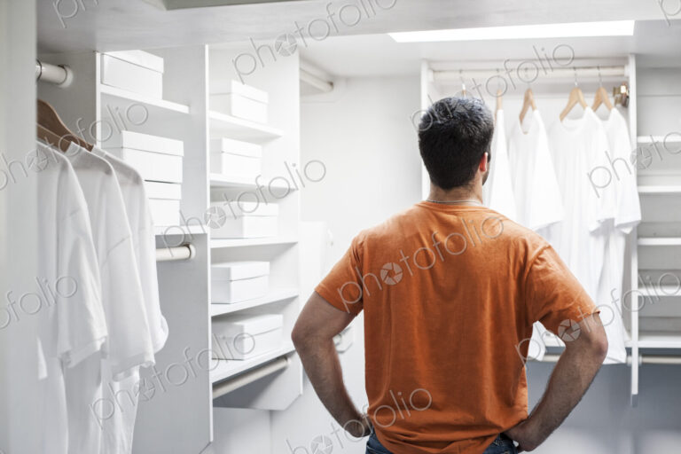 Hispanic man in a closet full of white clothes.
