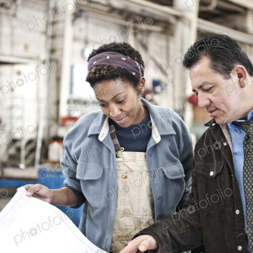 Hispanic man manager and black woman factory worker going over project plans in a… Hispanic man manager and black woman factory worker going over project plans in a…