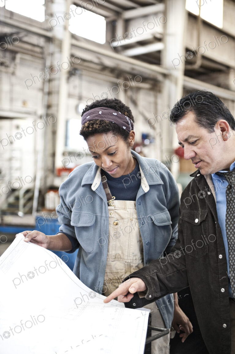 Hispanic man manager and black woman factory worker going over project plans in a…