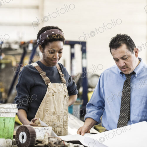 Hispanic man manager and black woman factory worker going over project plans in a…