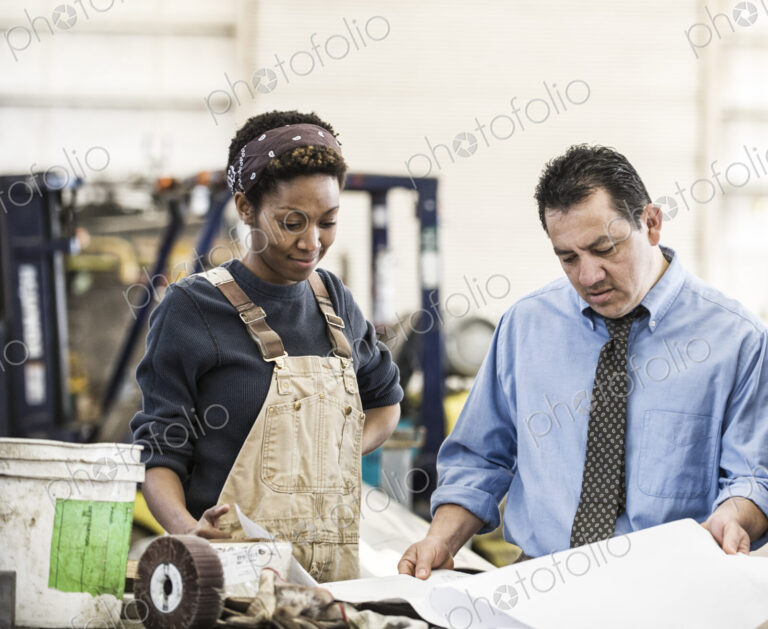 Hispanic man manager and black woman factory worker going over project plans in a…