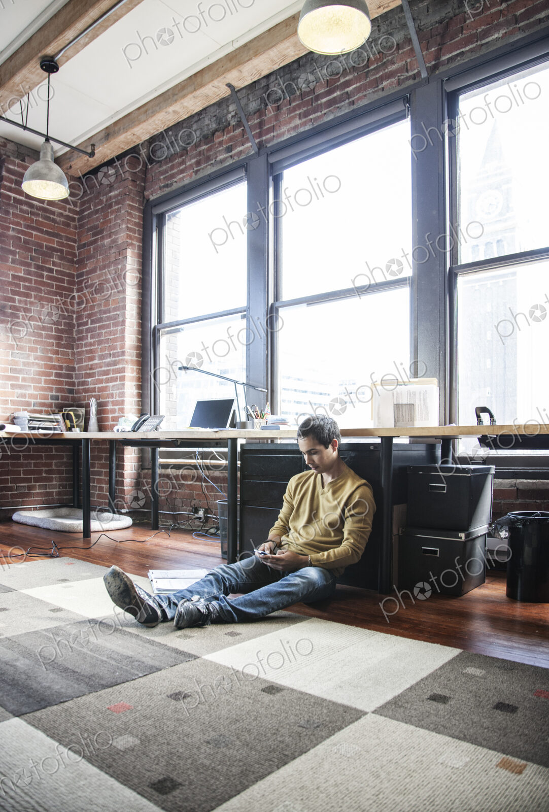 Hispanic man on his cell phone while sitting on floor at his office workstation.